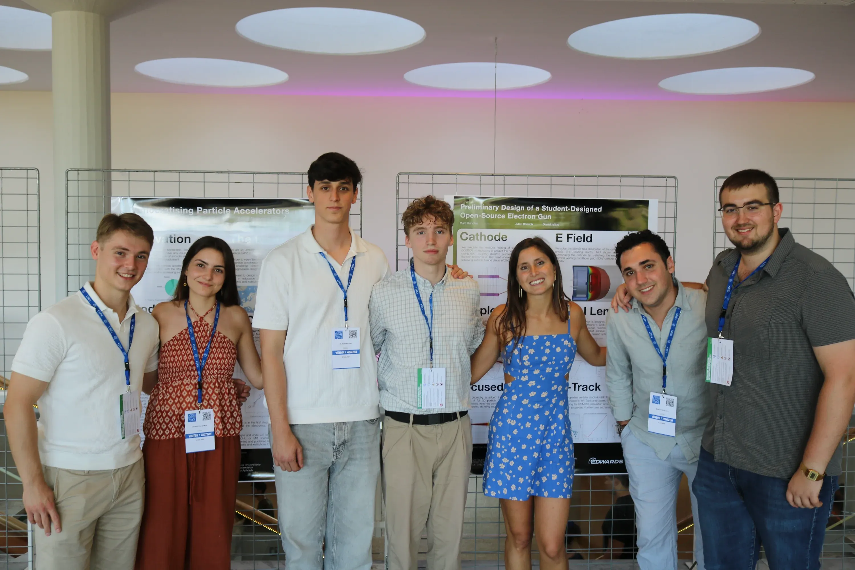 Seven team members with CERN visitor lanyards, smiling in front of their posters at CERN.